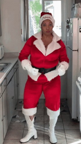 A Woman In A Santa Suit Is Standing In Front Of A White Refrigerator GIF