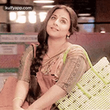A Woman In A Saree Is Holding A Shopping Bag And Smiling While Sitting Down . GIF