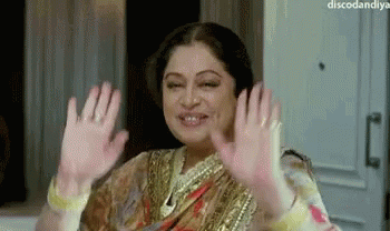 A Woman In A Sari Is Waving Her Hands In The Air And Smiling . GIF