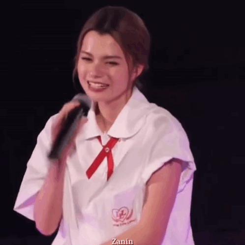 A Woman In A School Uniform Is Holding A Microphone And Smiling . GIF