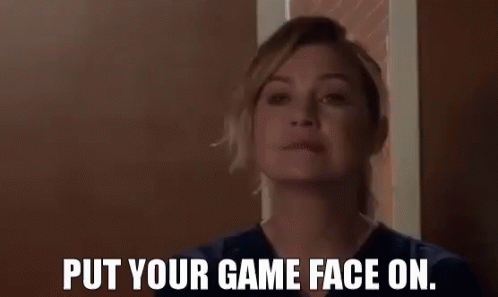 A Woman In A Scrub Top Is Standing In Front Of A Door And Says `` Put Your Game Face On . '' GIF