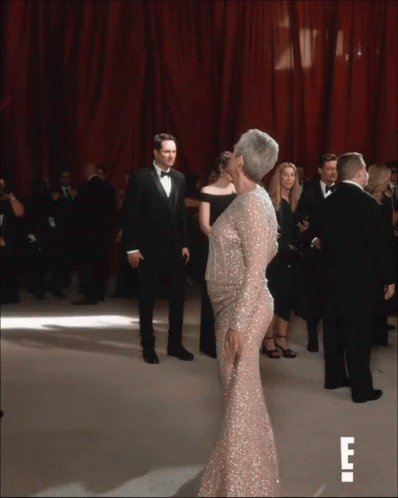 A Woman In A Sequined Dress Is Kissing A Man In A Tuxedo On A Red Carpet GIF