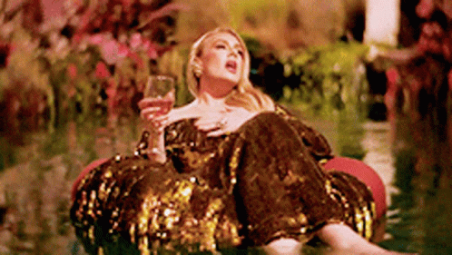 A Woman In A Sequined Dress Is Sitting On A Raft In The Water Holding A Glass Of Wine . GIF
