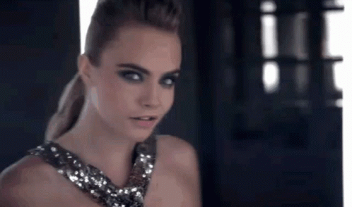 A Woman In A Sequined Dress Is Standing In Front Of A Window Looking At The Camera . GIF