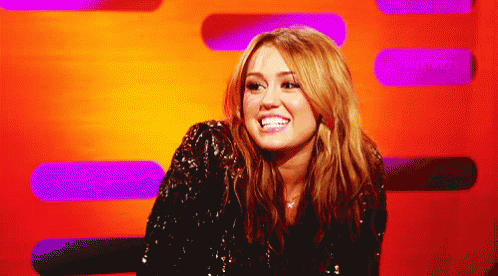 A Woman In A Sequined Jacket Smiles In Front Of A Purple And Orange Background GIF