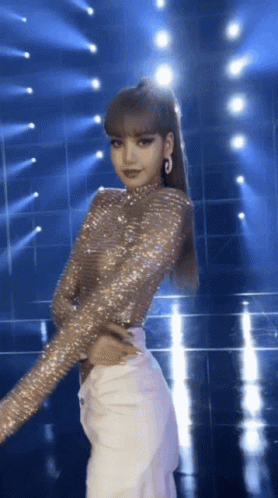 A Woman In A Sequined Top And White Pants Stands On A Stage GIF