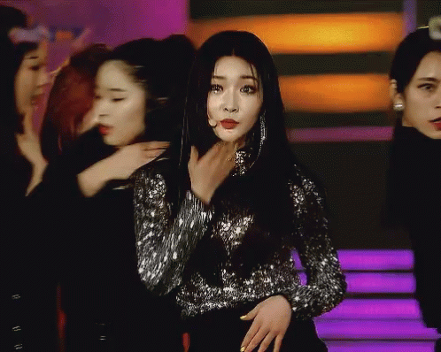 A Woman In A Sequined Top Stands In Front Of A Group Of Girls GIF