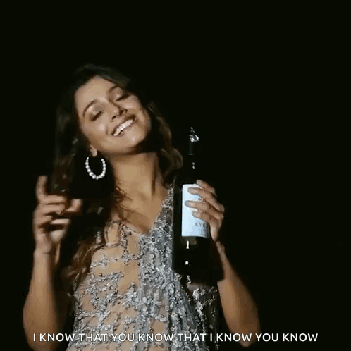 A Woman In A Sheer Dress Is Holding A Bottle Of Wine And Smiling . GIF