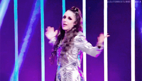 a woman in a silver dress is dancing on a stage in front of purple lights .