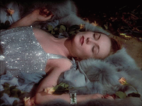 A Woman In A Silver Dress Laying On A Fur Blanket GIF