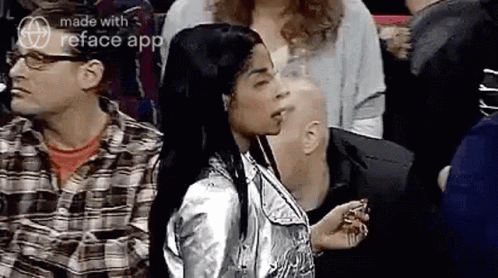 A Woman In A Silver Jacket Is Standing In A Crowd Of People And Smoking A Cigarette . GIF