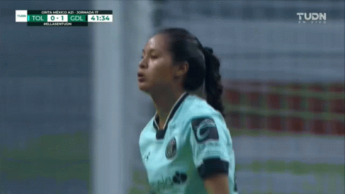 A Woman In A Soccer Uniform Stands In Front Of A Tv Screen That Says Tudn On It GIF