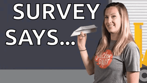 A Woman In A Sticker Giant Shirt Holds A Paper Airplane In Front Of A Sign That Says Survey Says GIF