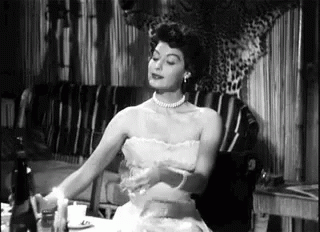 A Woman In A Strapless Dress Is Sitting At A Table With A Candle . GIF