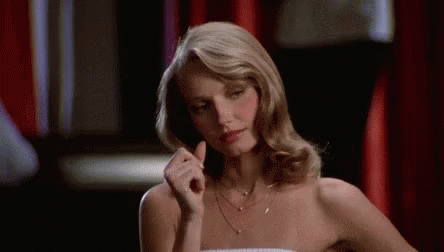 A Woman In A Strapless Dress Is Sitting At A Table With Her Hand In Her Hair . GIF
