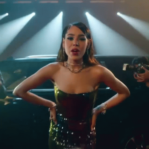 A Woman In A Strapless Dress Is Standing In Front Of A Car On A Stage . GIF