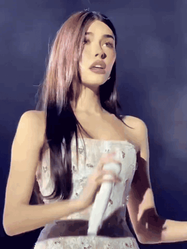 A Woman In A Strapless White Dress Is Holding A Microphone GIF