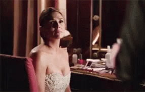 A Woman In A Strapless White Dress Is Sitting In Front Of A Mirror . GIF