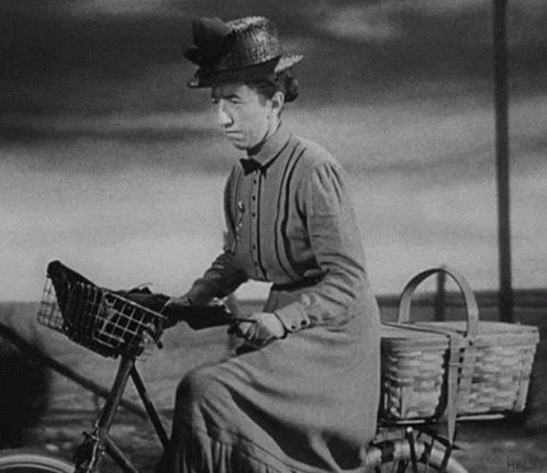 A Woman In A Straw Hat Is Riding A Bicycle GIF