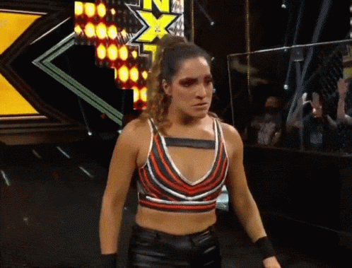 A Woman In A Striped Crop Top Is Standing In Front Of A Sign That Says Nxt On It GIF
