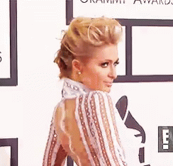A Woman In A Striped Dress Is Standing On A Red Carpet At An Event . GIF