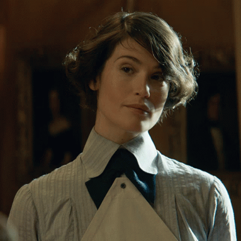 A Woman In A Striped Shirt And Tie Looks At The Camera GIF