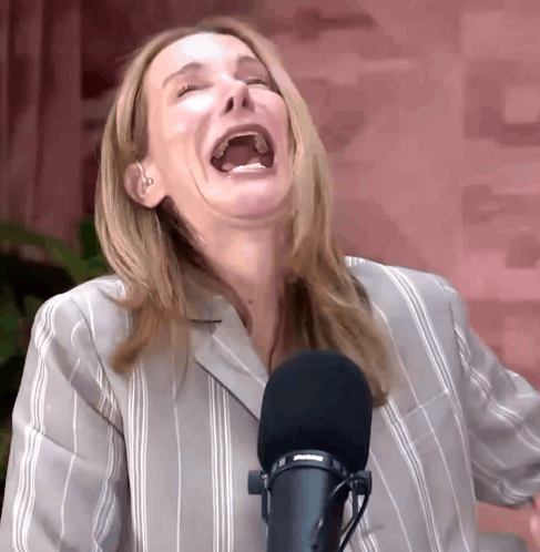 A Woman In A Striped Shirt Is Laughing In Front Of A Microphone GIF