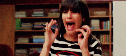 A Woman In A Striped Shirt Is Screaming And Holding A Cell Phone In Her Hand . GIF