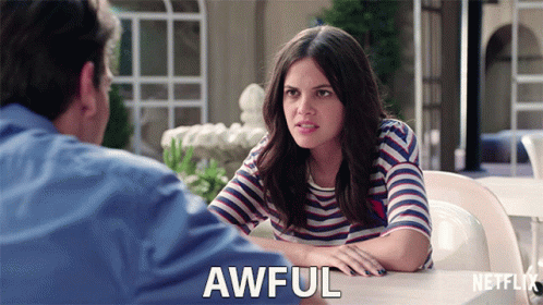 A Woman In A Striped Shirt Is Sitting At A Table With A Man And Says Awful In Front Of Her GIF