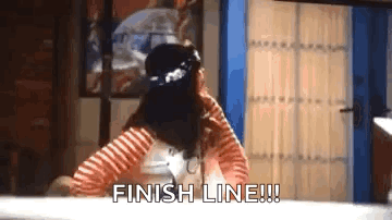 A Woman In A Striped Shirt Is Sitting At A Table With Her Hands On Her Head And Says `` Finish Line '' . GIF