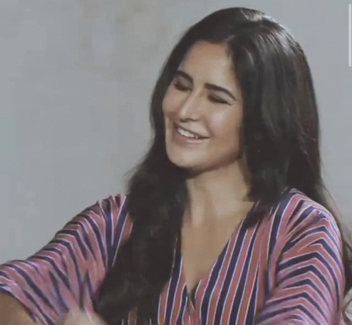 A Woman In A Striped Shirt Is Smiling And Looking Down GIF