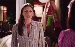 A Woman In A Striped Shirt Is Talking To Another Woman In A Living Room . GIF
