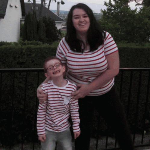 A Woman In A Striped Shirt Stands Next To A Young Boy GIF