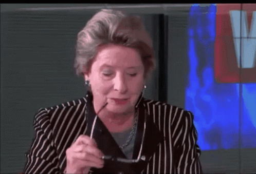 A Woman In A Striped Suit Holds A Pair Of Glasses In Her Hand GIF