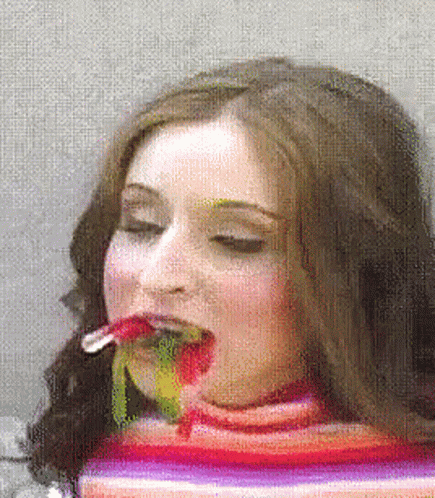 A Woman In A Striped Sweater Is Eating A Rainbow Colored Lollipop GIF