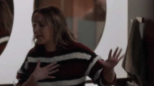 A Woman In A Striped Sweater Is Looking At Herself In A Mirror GIF