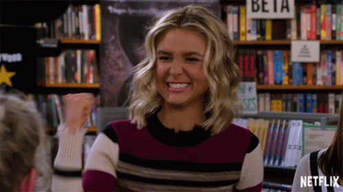 Woman In Striped Sweater Smiling In Front Of Beta Sign GIF