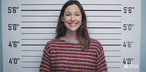 A Woman In A Striped Sweater Is Smiling In Front Of A Police Line Up That Says Netflix GIF