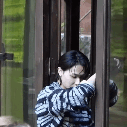 A Woman In A Striped Sweater Is Standing In Front Of A Glass Door . GIF