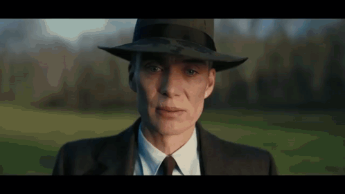A Woman In A Suit And Hat Is Looking At The Camera . GIF