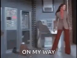 A Woman In A Suit And Red Pants Is Standing In A Room With The Words On My Way Written On The Floor . GIF