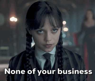A Woman In A Suit And Tie Is Looking At The Camera With The Words `` None Of Your Business '' Written Below Her . GIF