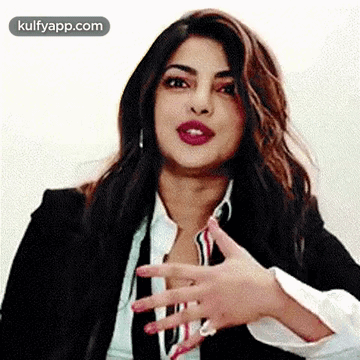 A Woman In A Suit And Tie Is Making A Funny Face With Her Hand . GIF