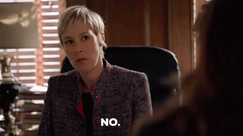 A Woman In A Suit And Tie Is Sitting In A Chair And Says No . GIF