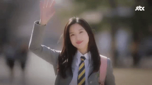 A Woman In A Suit And Tie Is Waving Her Hand . GIF