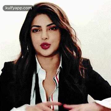 A Woman In A Suit And White Shirt Is Making A Gesture With Her Hands . GIF