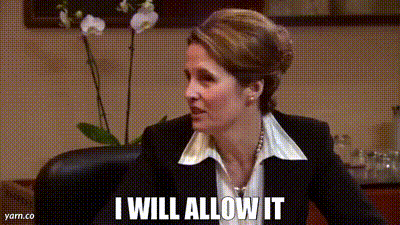 A Woman In A Suit And White Shirt Is Sitting In A Chair And Saying I Will Allow It . GIF