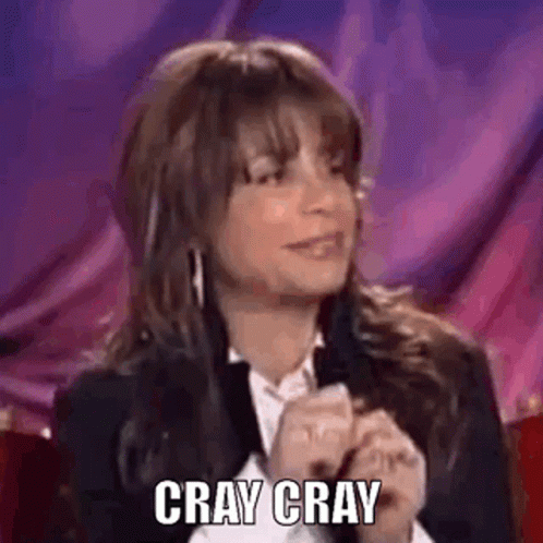 A Woman In A Suit And White Shirt Is Sitting In Front Of A Purple Curtain And Says `` Cray Cray '' . GIF