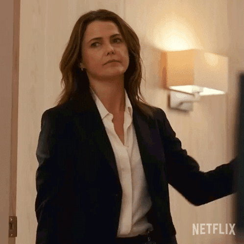 A Woman In A Suit And White Shirt Is Standing In A Room . GIF