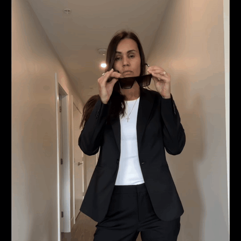 A Woman In A Suit Is Adjusting Her Sunglasses In A Hallway GIF